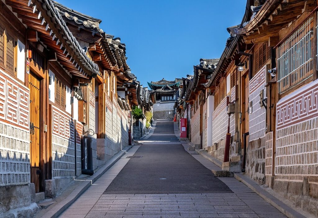 Tiled hanok rooftops along a Bukchon Hanok Village street under blue sky in Seoul