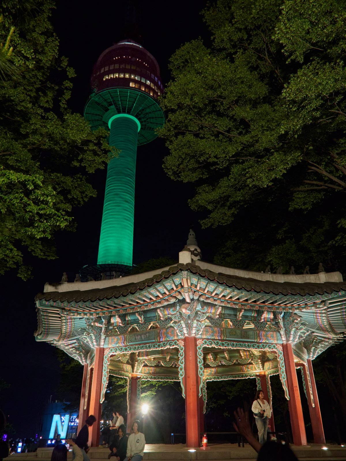 N Seoul Tower lit up after dark with a traditional pavilion roof in the foreground