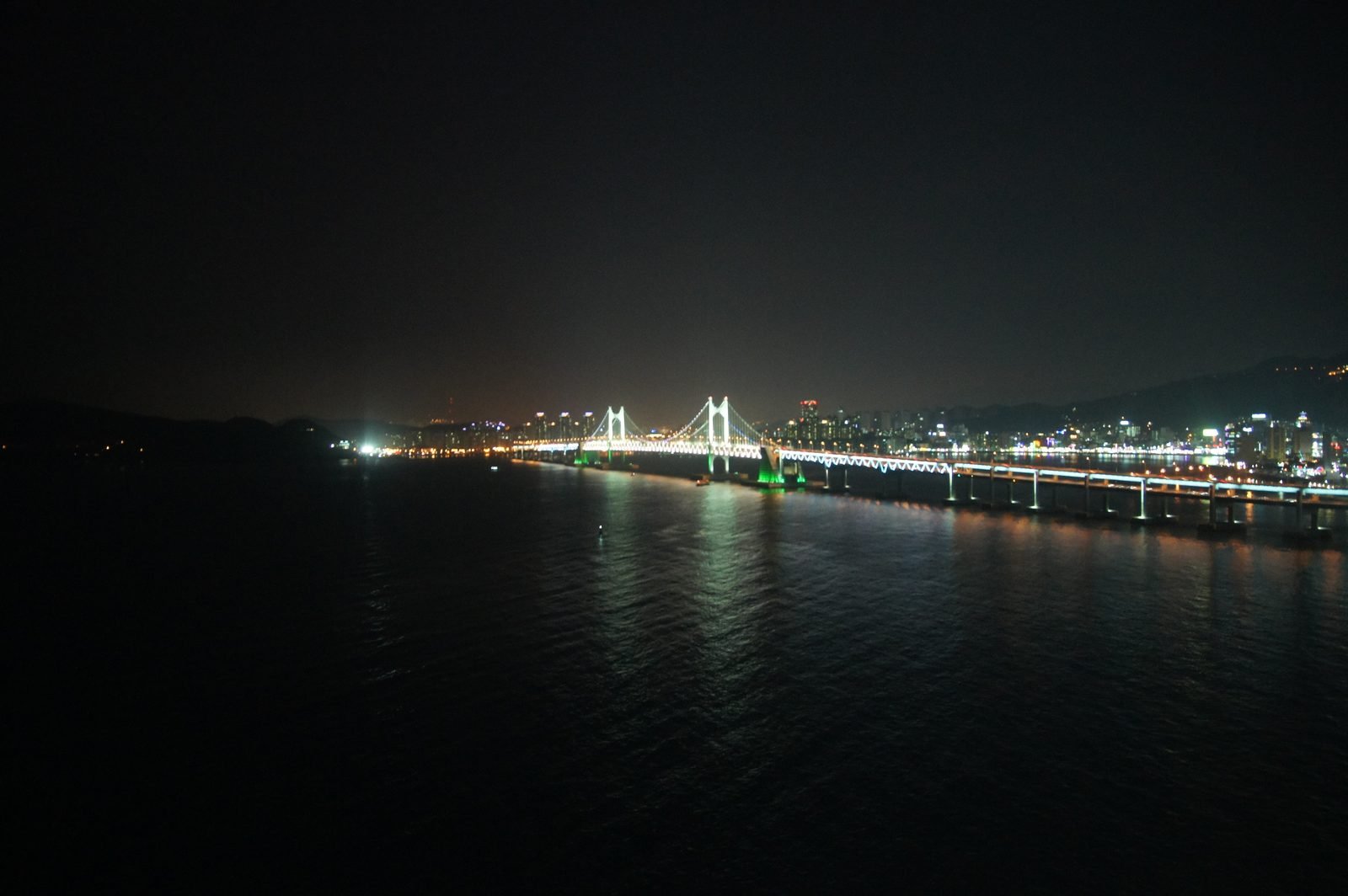 Gwangan Bridge lit in changing colors above the water at night in Busan
