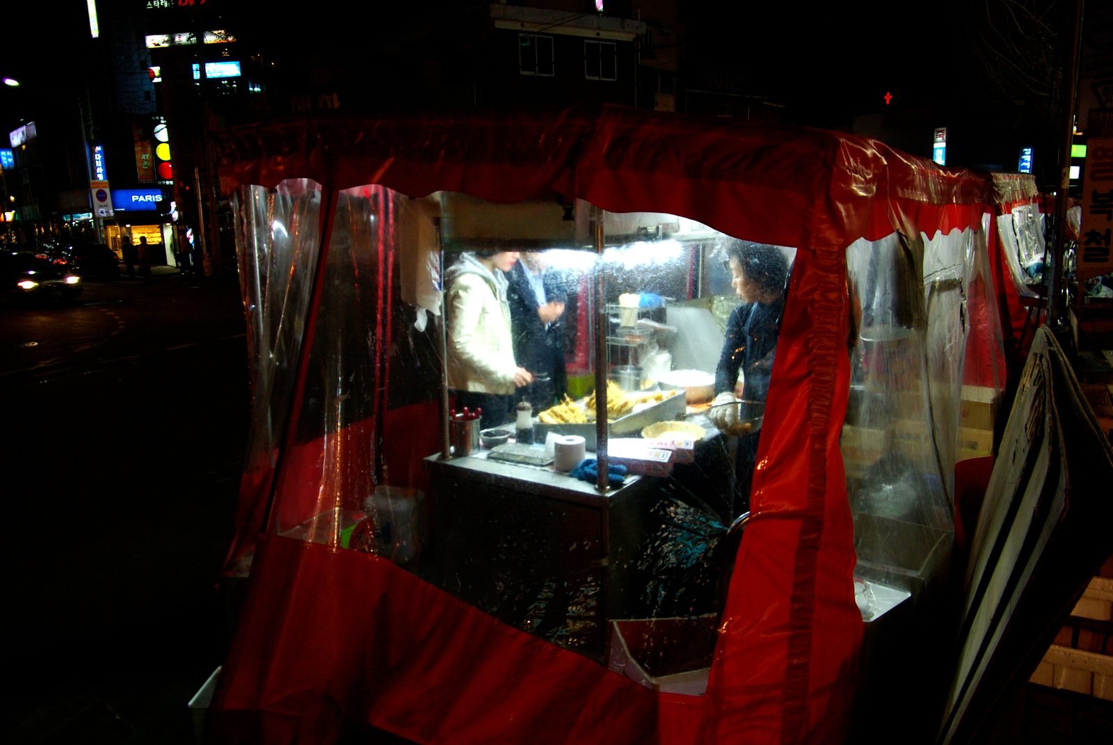 Customers standing at a lit street food stall in Seoul in the evening