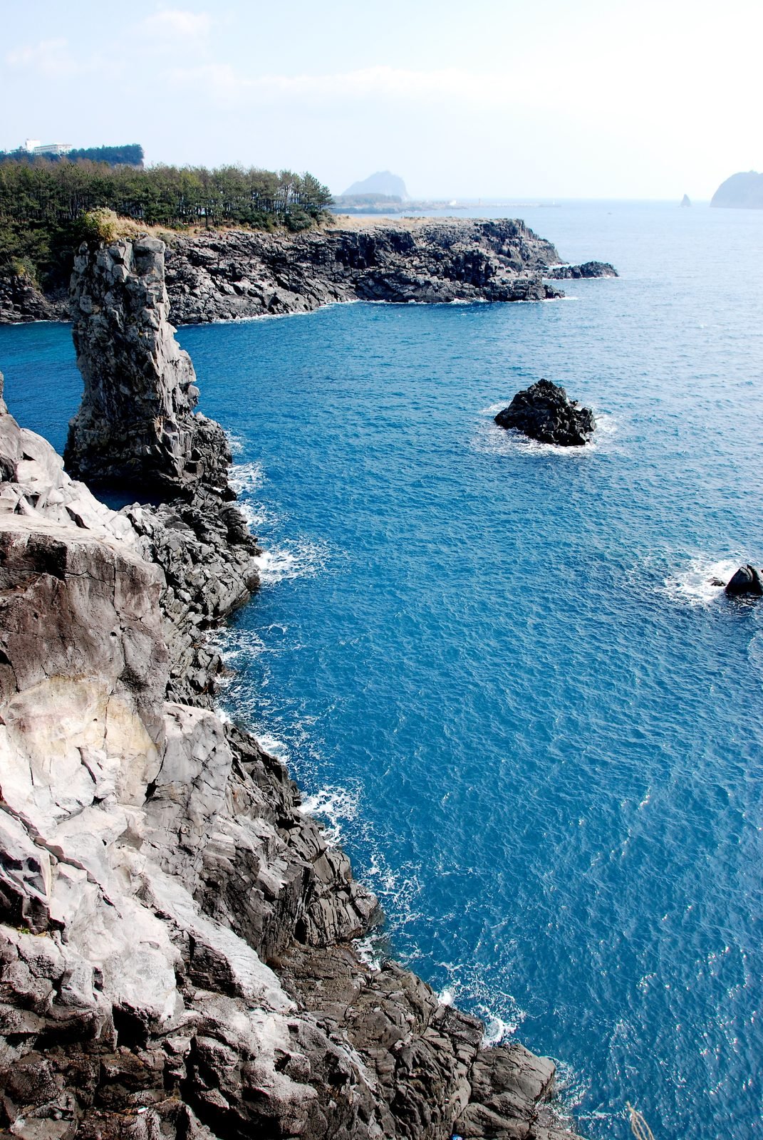 Dark volcanic rock stacks and cliffs dropping into deep blue water on Jeju Island